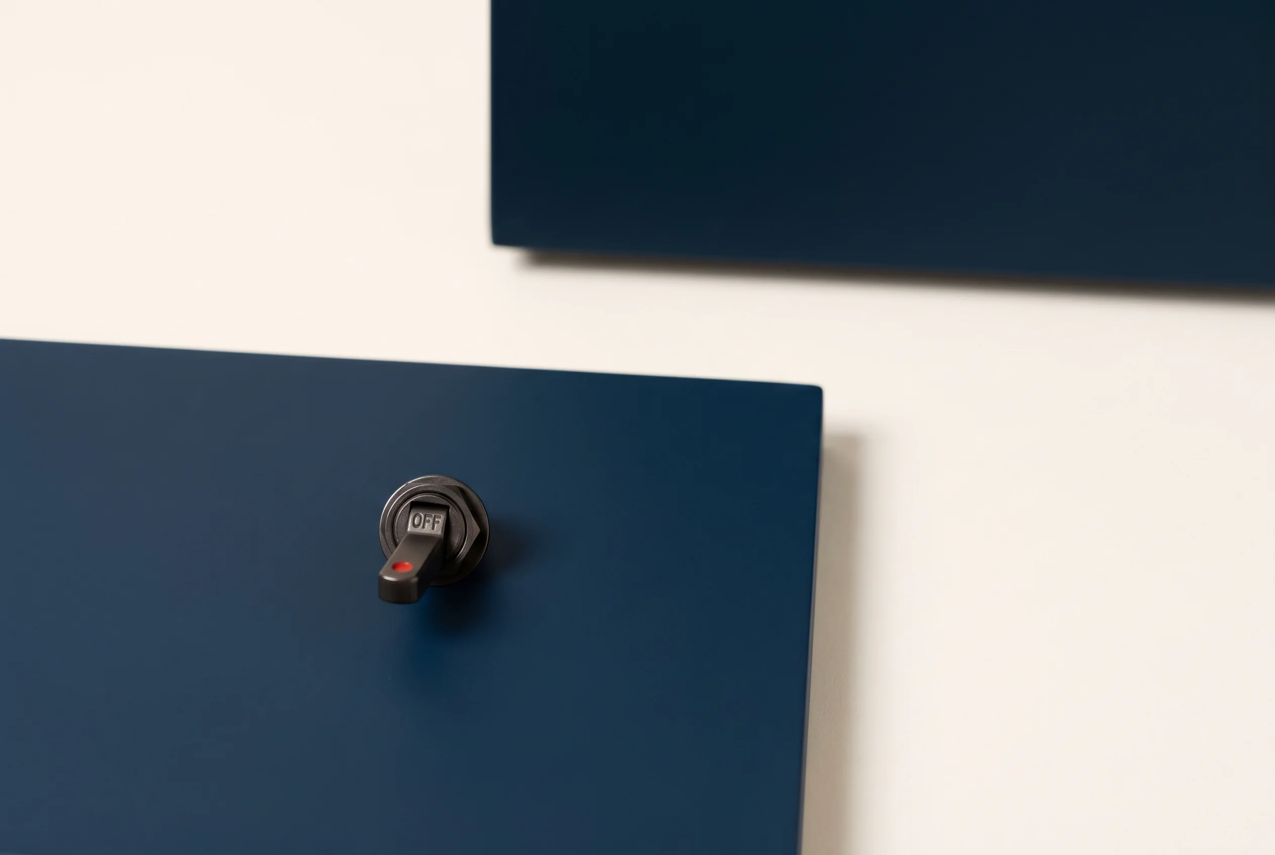 A black toggle switch marked OFF, with a small red indicator, on a navy panel, a second identical panel out of focus behind it, standing for a switch you own and can turn off.