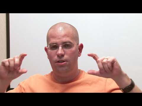 A man in glasses and an orange T-shirt talks to the camera in front of a whiteboard, in Google's short video on meta keywords tags.